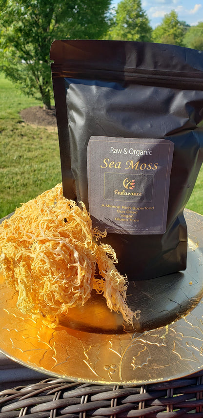 Black 8 oz pouch of Premium Organic Dried Gold Sea Moss on a round table with dried sea moss in front and lawn and trees in the background